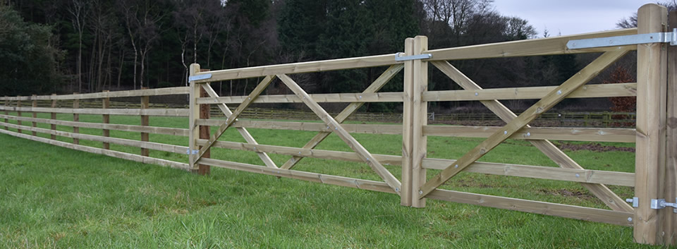 Timber double gates next to post and rail fencing in green field